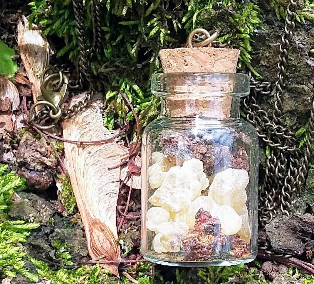 Small glass bottle of frankincense and myrrh with a cord closure on an oxidized brass chain